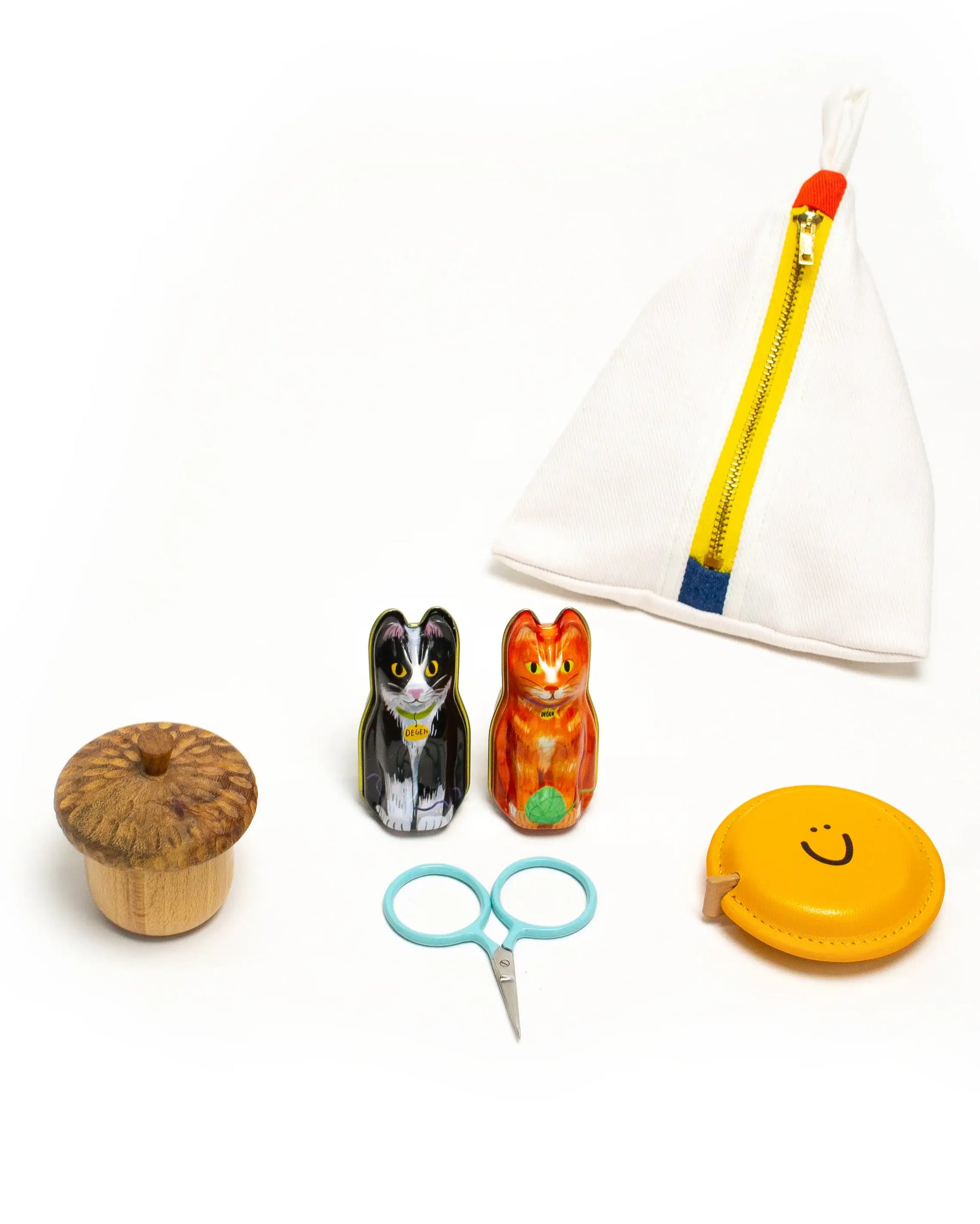 Collection of small items including a wooden bobbin, cat-shaped container, orange cat figurine, scissors, yellow tape measure, and white pouch with pencil.