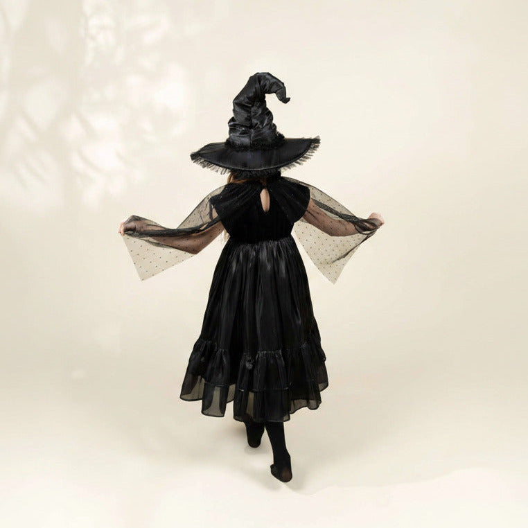 Person wearing a black witch costume with a hat on a plain background