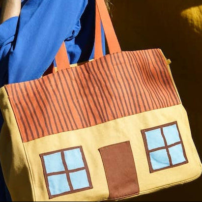 Person holding a house-shaped bag against a warm-toned background