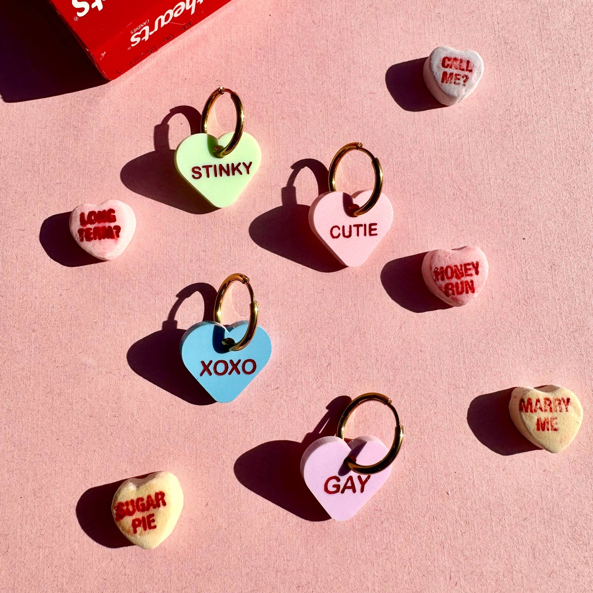 Heart-shaped keychains with various text on a pink background, resembling conversation hearts.