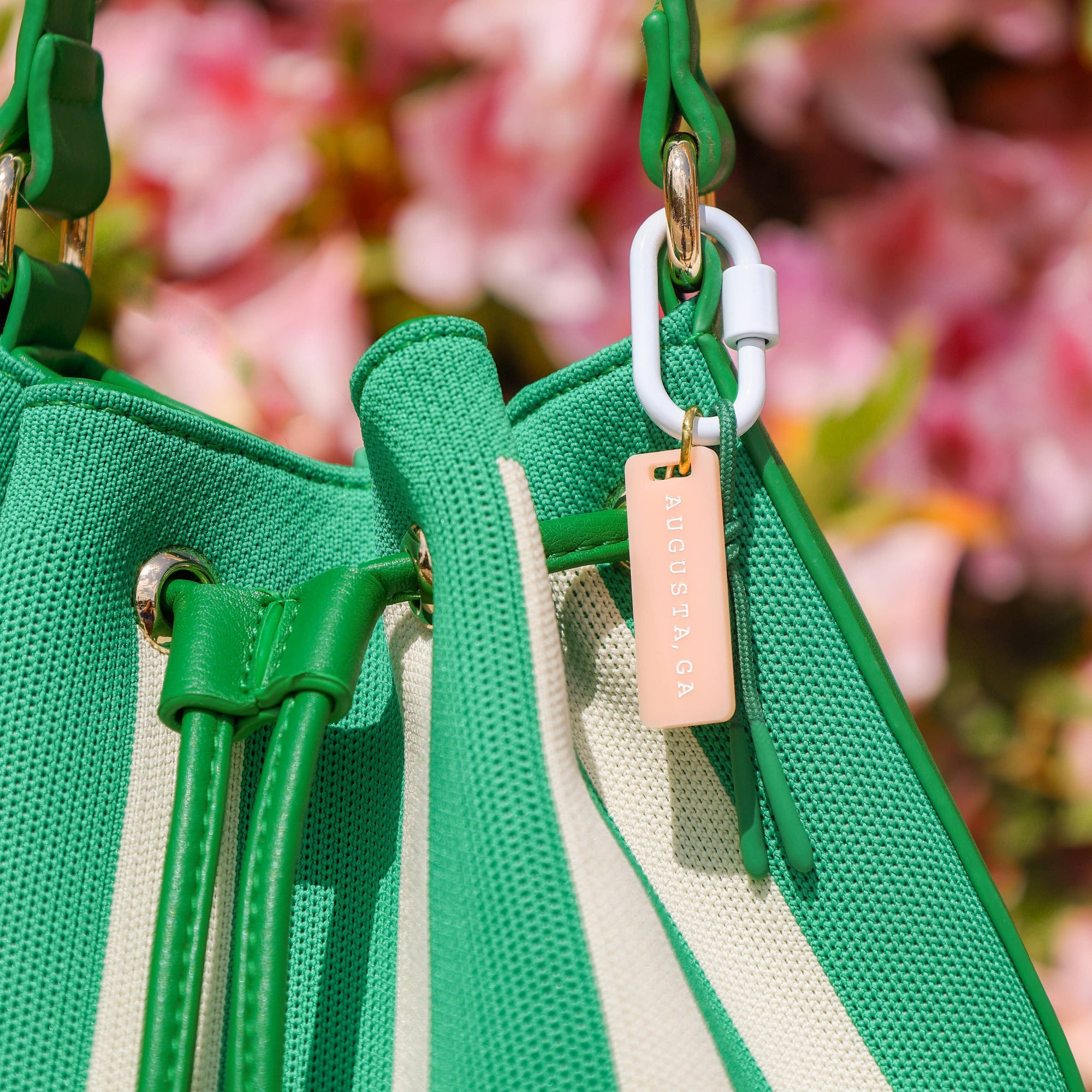 Green and beige striped bag with a pink tag against a blurred floral background