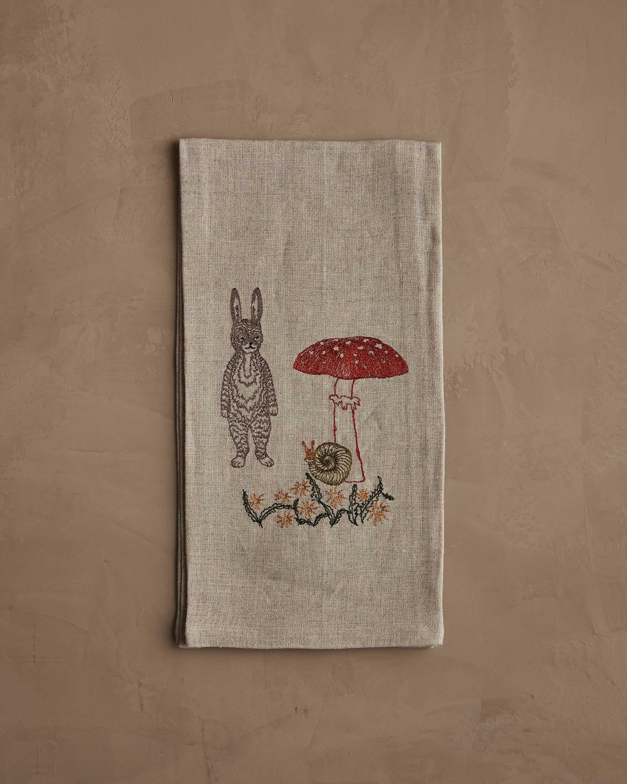 Textile with embroidered design of a rabbit and mushroom on a beige background