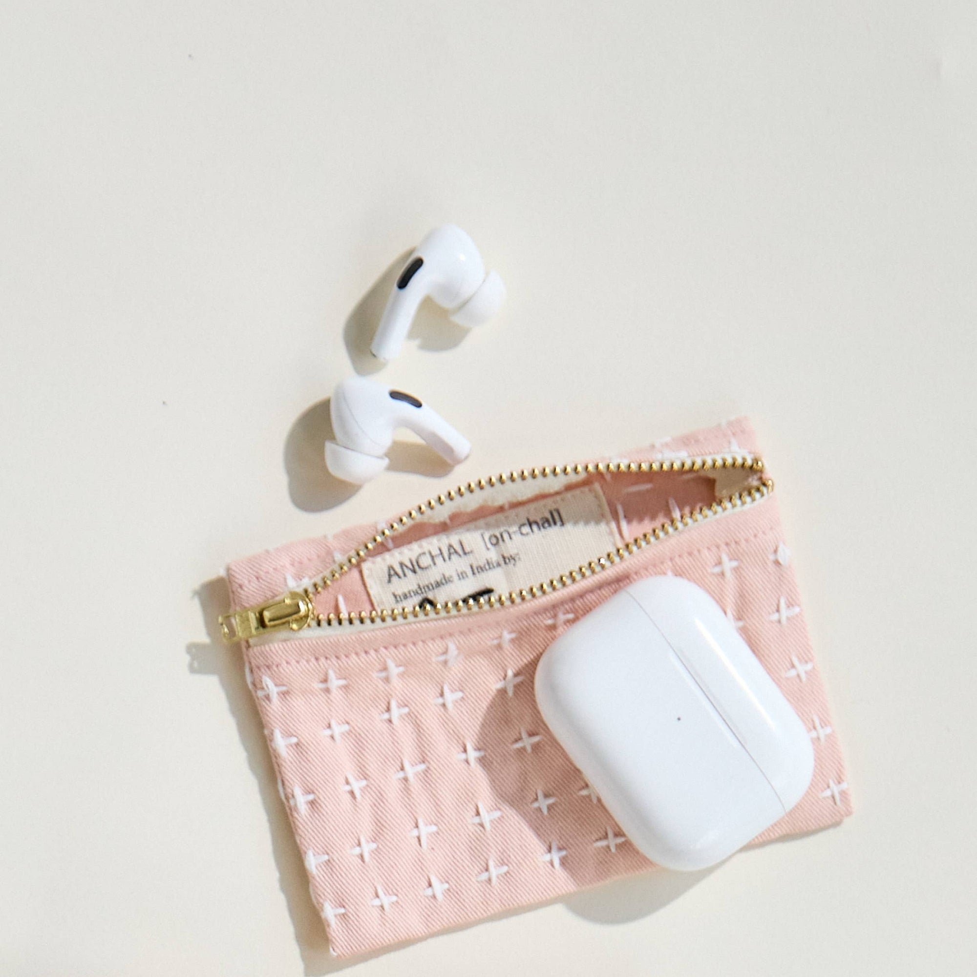White wireless earbuds in a pink pouch with gold zipper on a light beige background