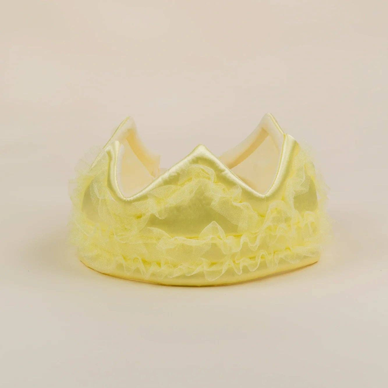A pale yellow ruffled crown or tiara with a sheer mesh texture and satin trim, photographed on a plain light beige background.