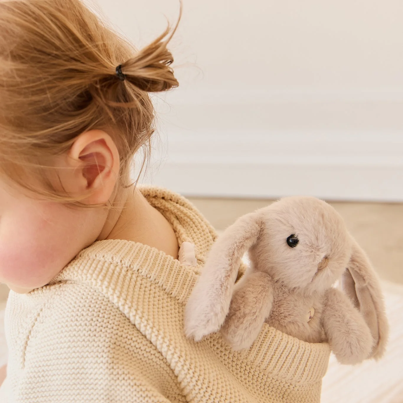 Child holding a fluffy toy rabbit against a neutral background
