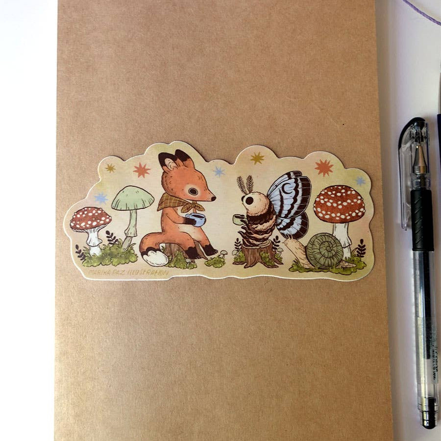 Sticker of a fox and butterfly on a brown notebook with a pen and yarn in the background.
