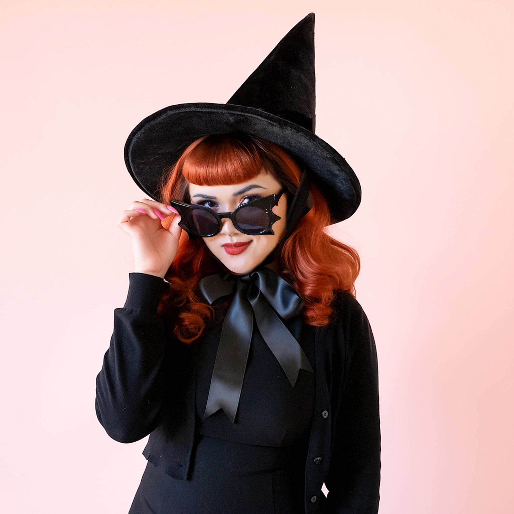 Person in a black witch costume with sunglasses on a pink background