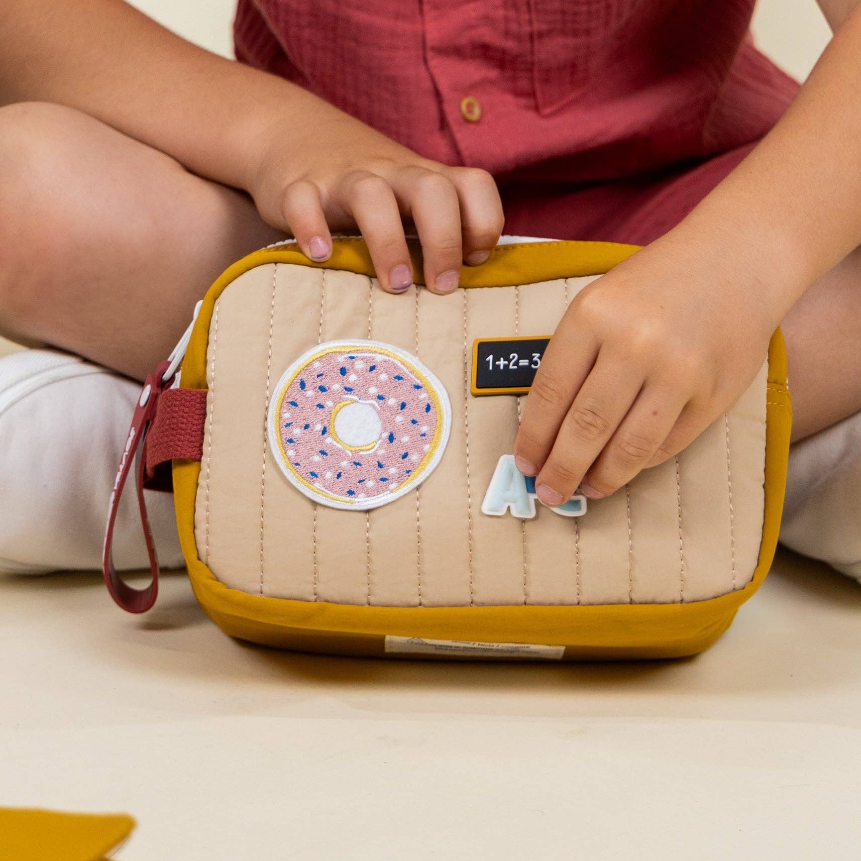 Child holding a small beige bag with colorful patches on a light background
