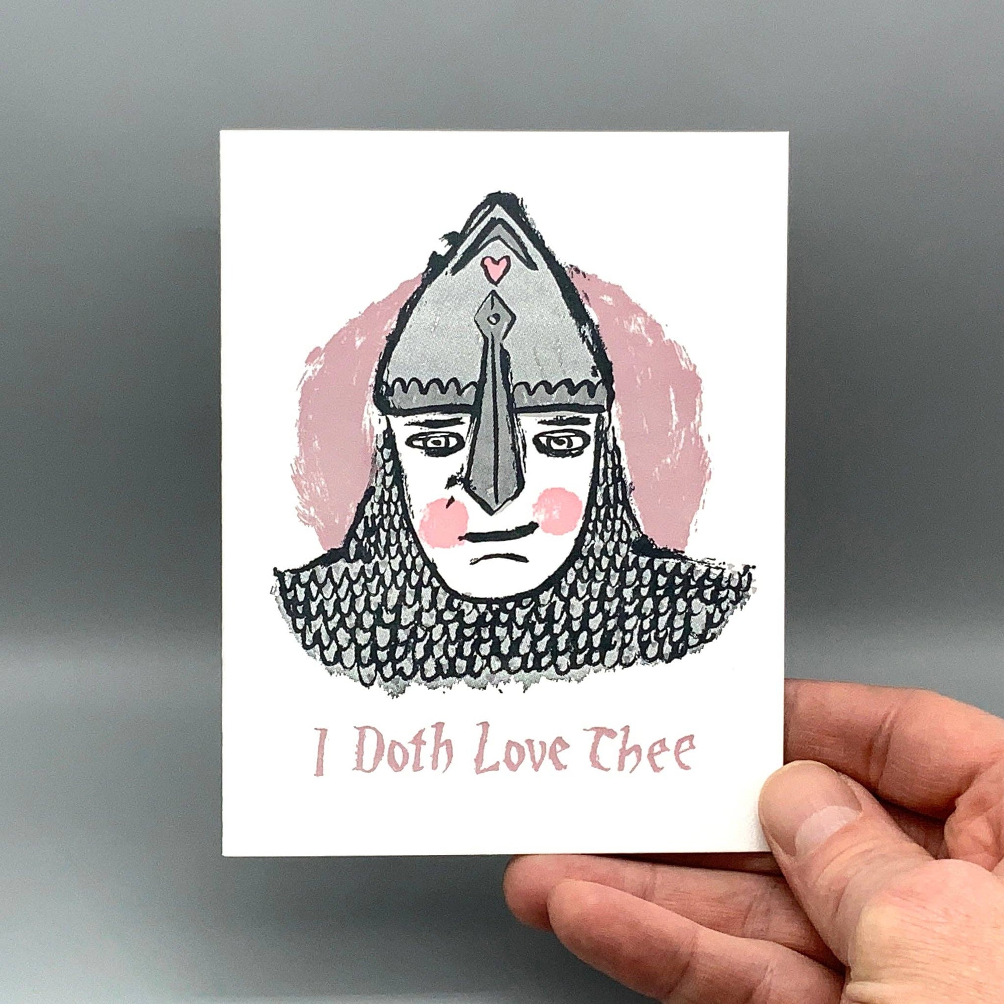 Card with a Viking helmet illustration and 'I Doth Love Thee' text held by a hand against a gray background