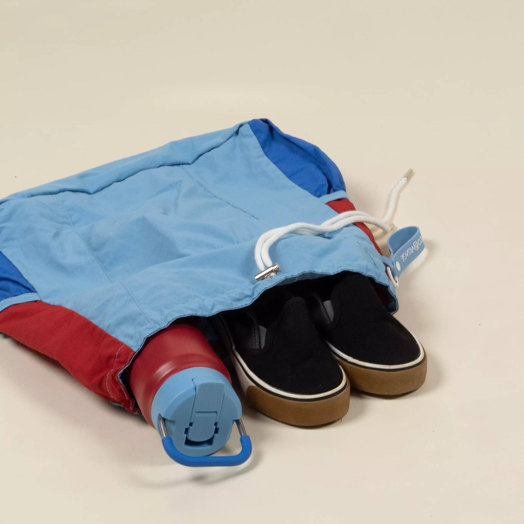 Blue and red bag with a black sneaker inside on a beige background