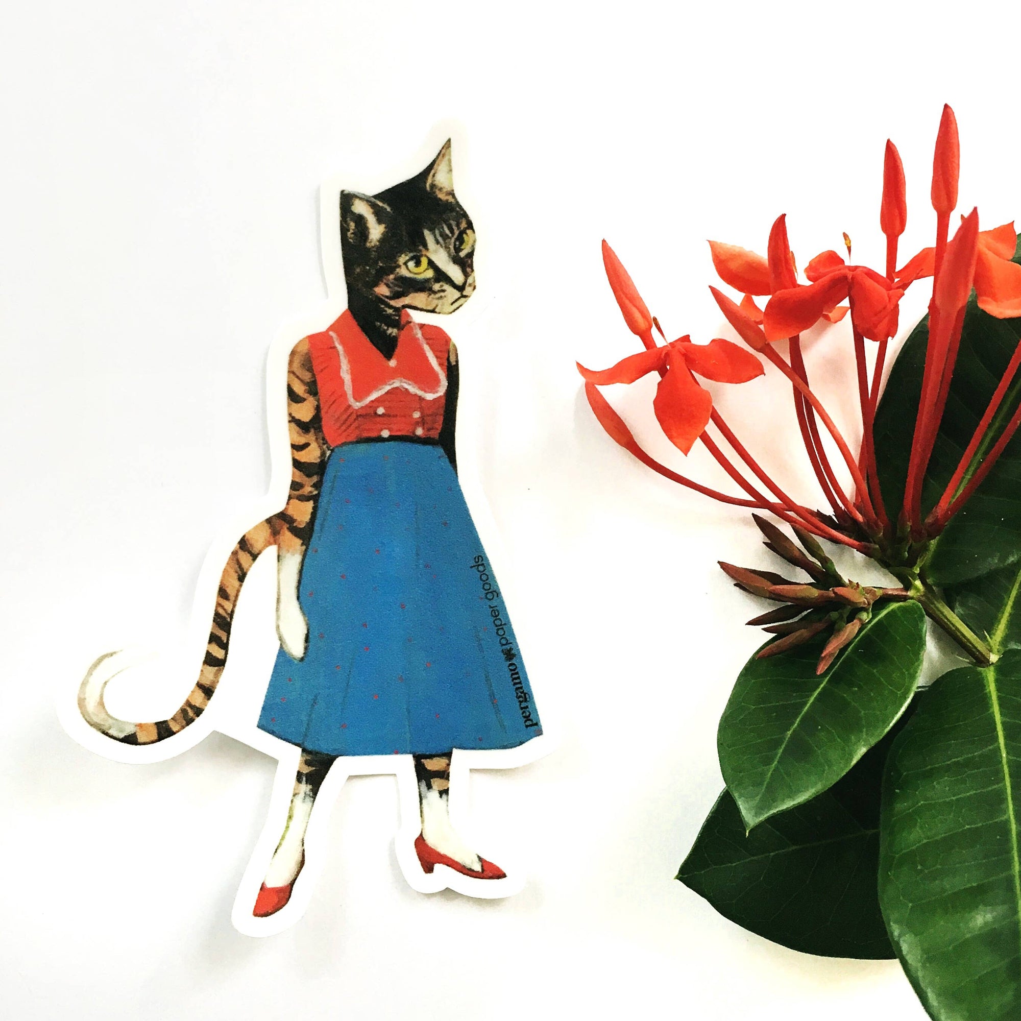 Cat-shaped paper cutout wearing a dress next to a red flower