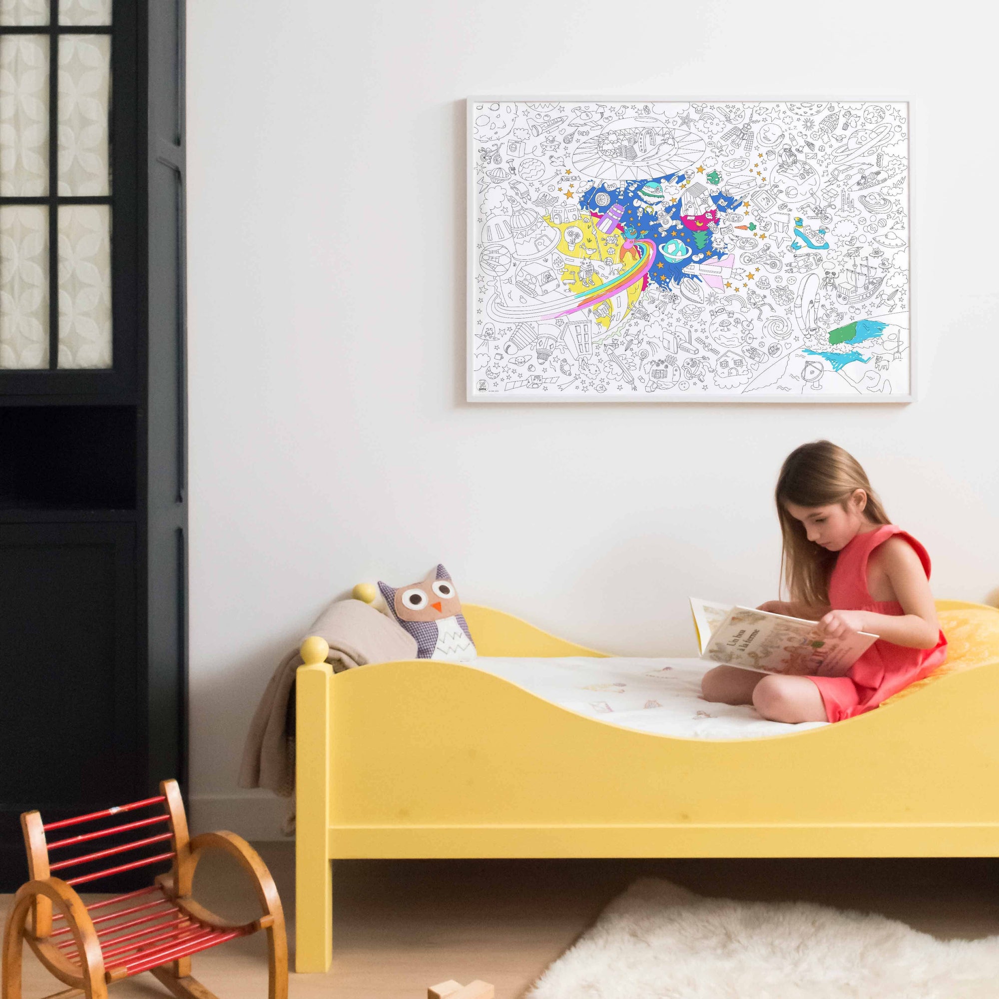Child reading a book on a yellow bed with a colorful abstract painting on the wall.