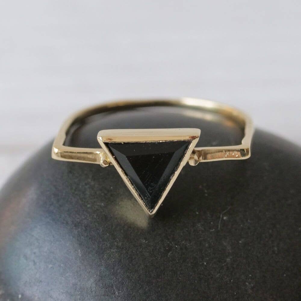 Gold ring with a black triangle stone on a dark surface