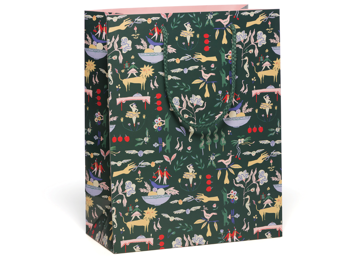 A tall gift bag with a dark green background and an all-over whimsical pattern featuring birds, deer, flowers, and small illustrated figures in pink, yellow, red, and light blue. The bag has a light pink inner lining and matching printed handles, shown on a clean white background.