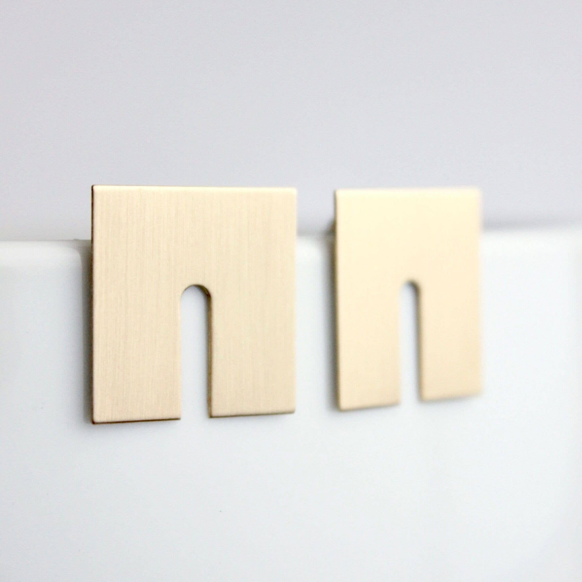 Gold square earrings on a light gray background