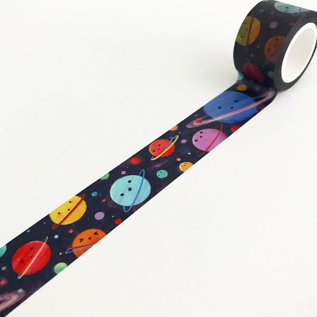 A roll of decorative tape with a colorful space pattern, unrolled diagonally on a plain white background. The tape features cartoon planets in red, orange, yellow, blue, purple, and green on a dark navy background.
