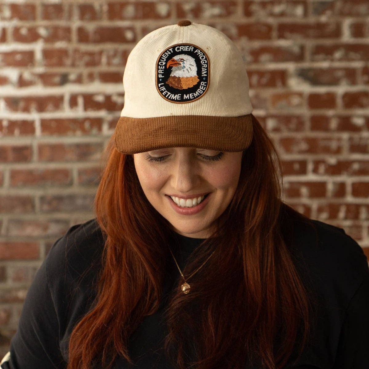 Person wearing a cap with a logo against a brick wall