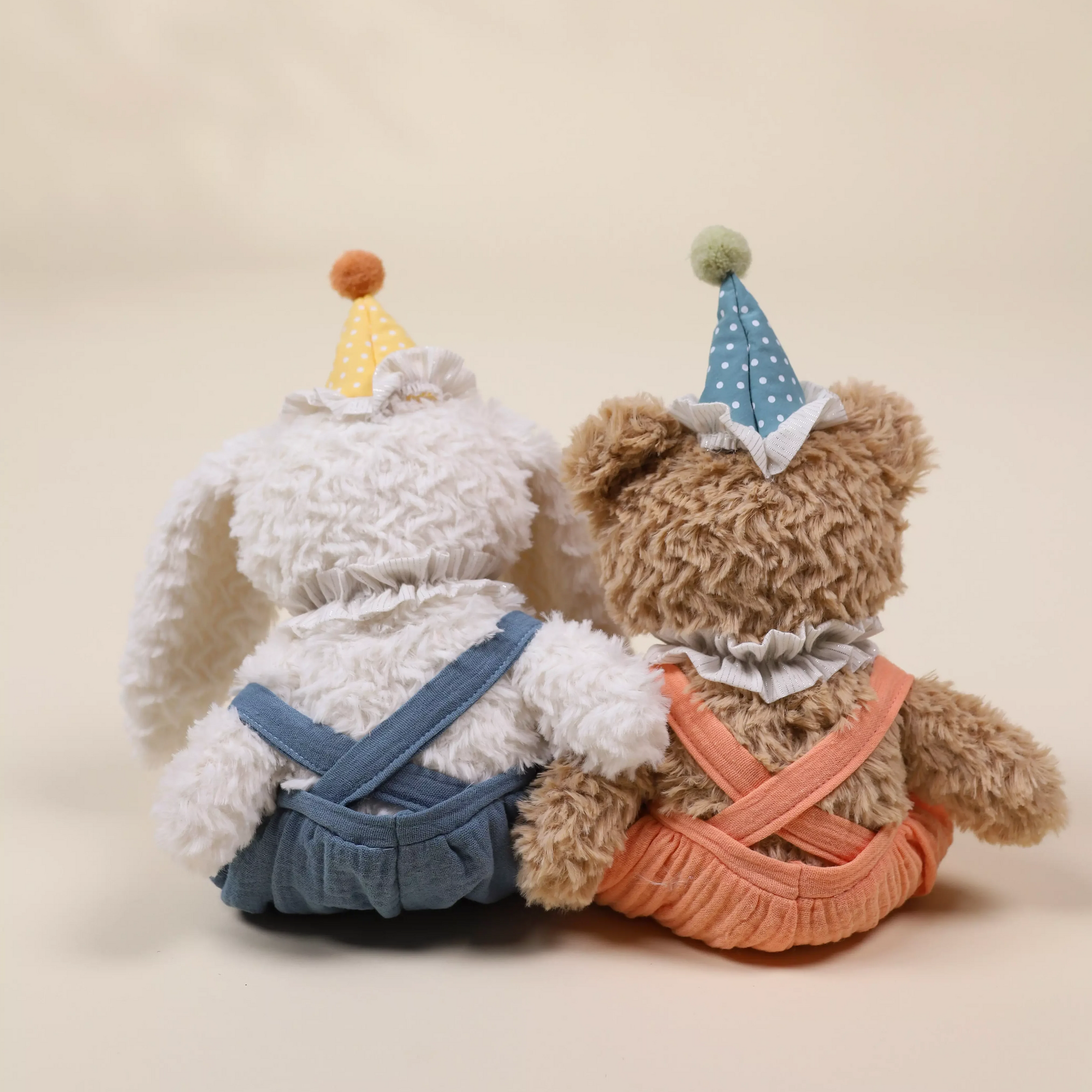Two teddy bears wearing party hats and outfits on a beige background
