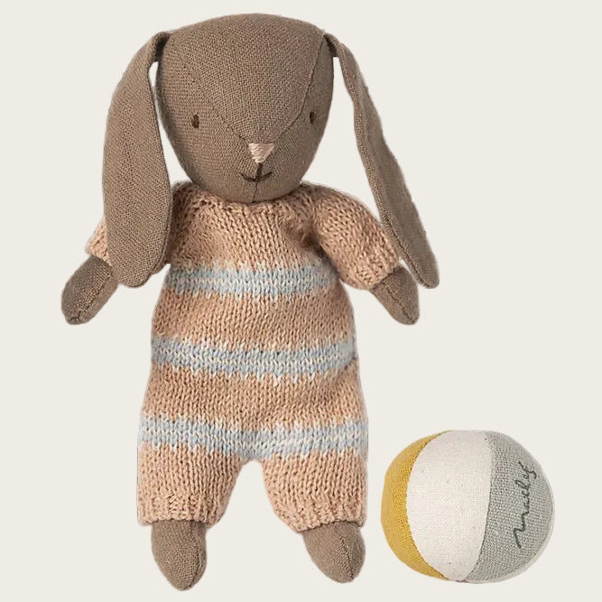 A handmade plush bunny doll with long floppy ears, wearing a knitted peach and white striped romper, shown next to a small striped ball on a gray and white checkered background.