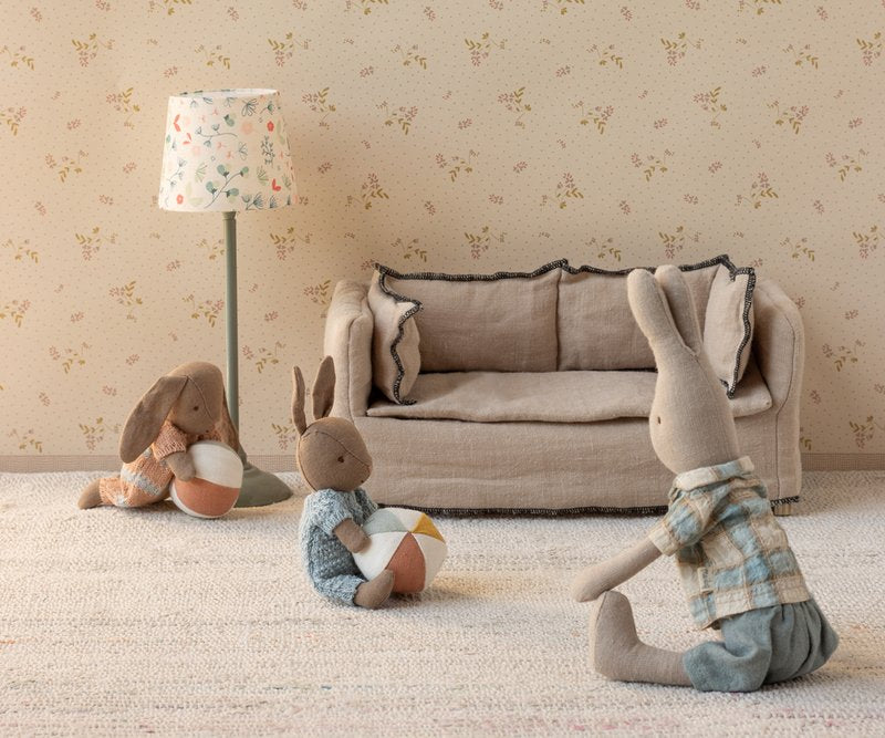 Three plush rabbit toys in a living room setting with a sofa and lamp.