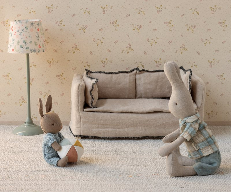 Two stuffed rabbits in a room with a sofa and lamp.