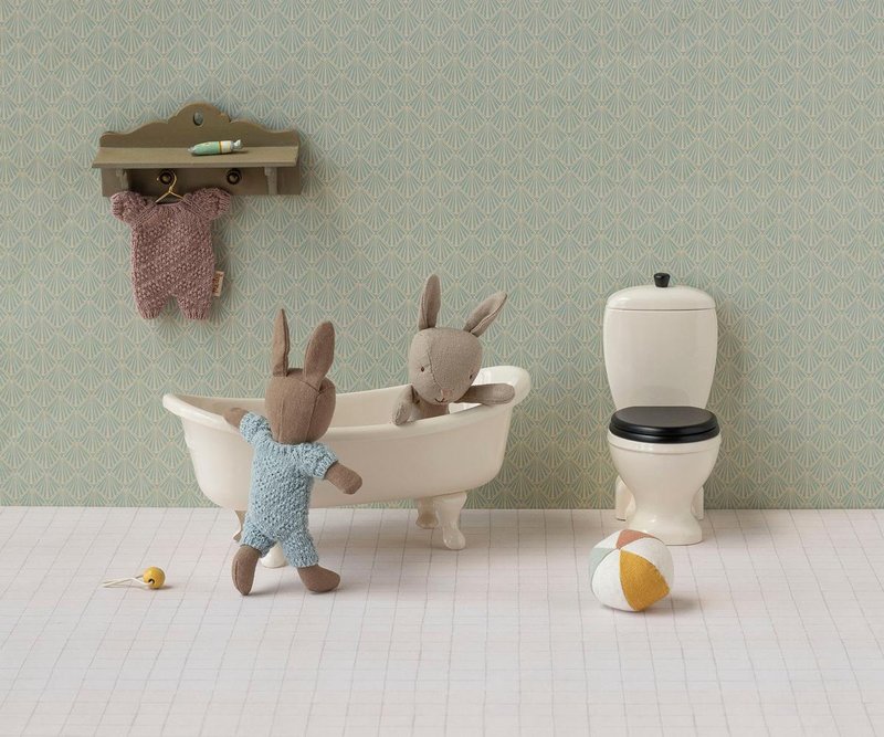 Two stuffed rabbit toys in a bathroom setting with a bathtub and toilet.