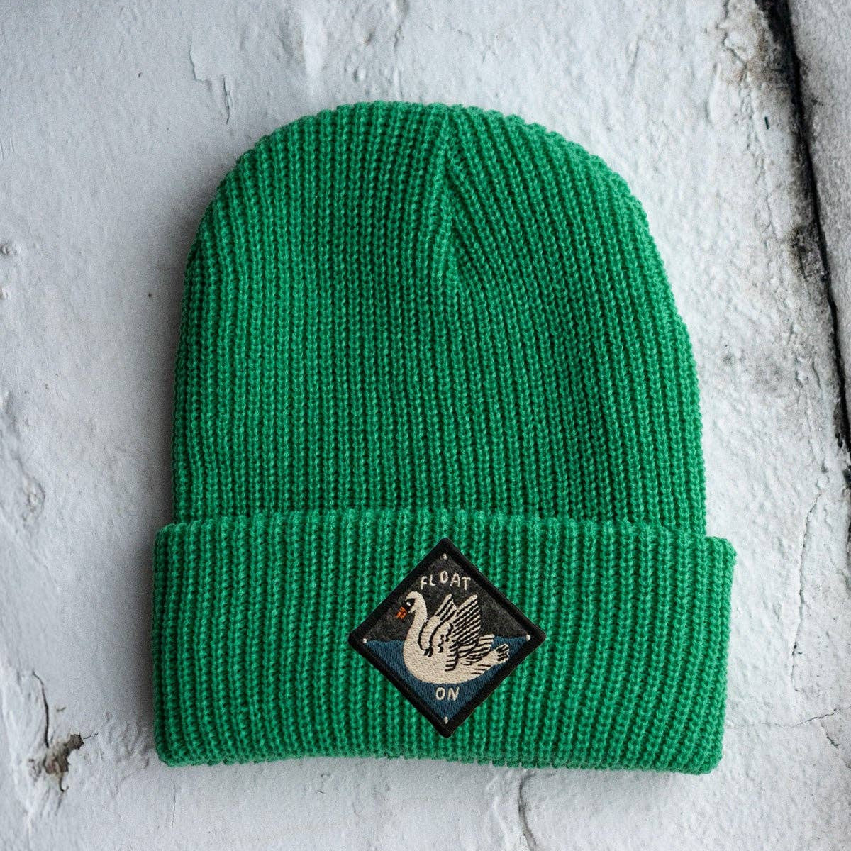 Green beanie with a logo patch on a textured white background
