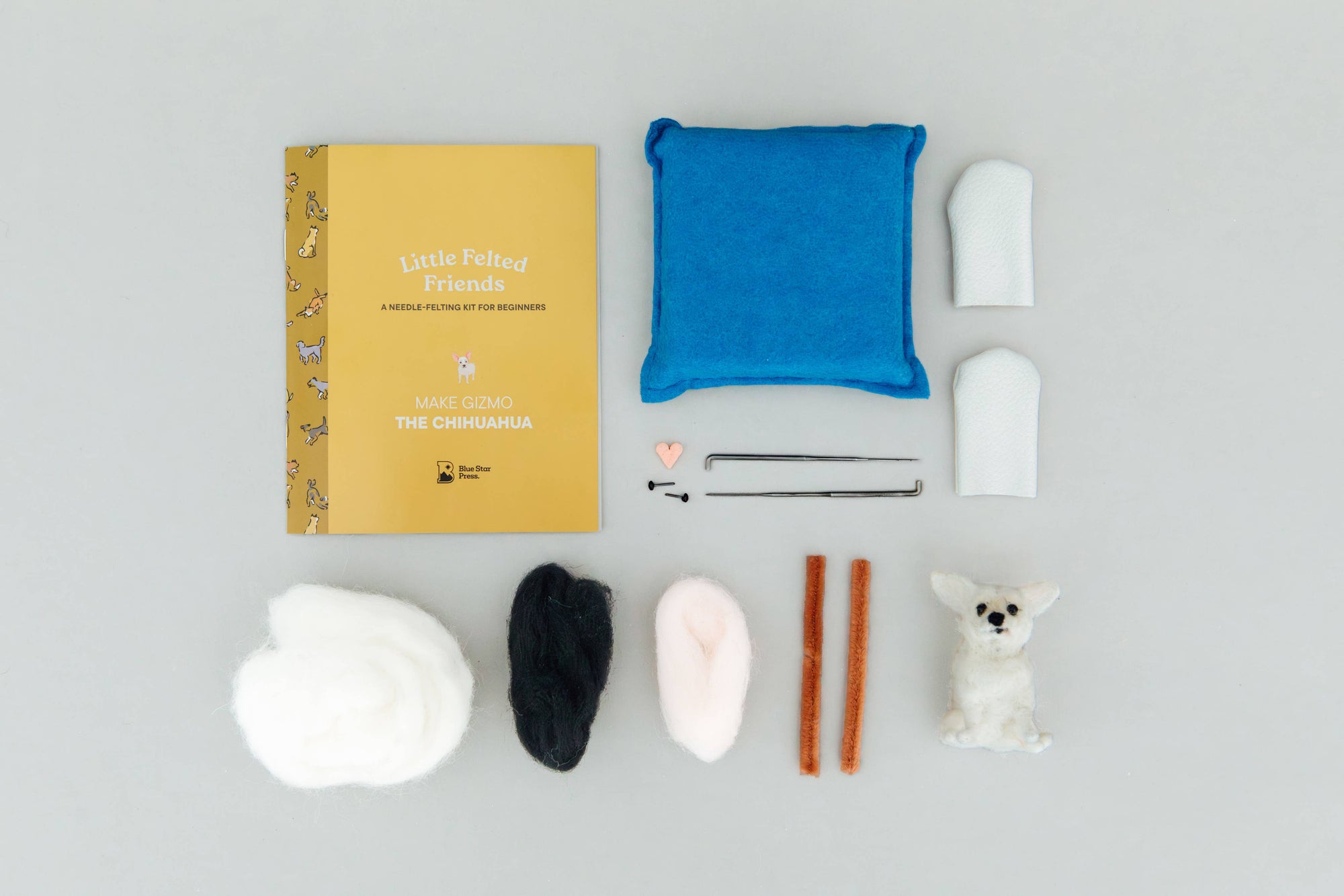 Collection of craft materials including a book, fabric pieces, and small figures on a gray background