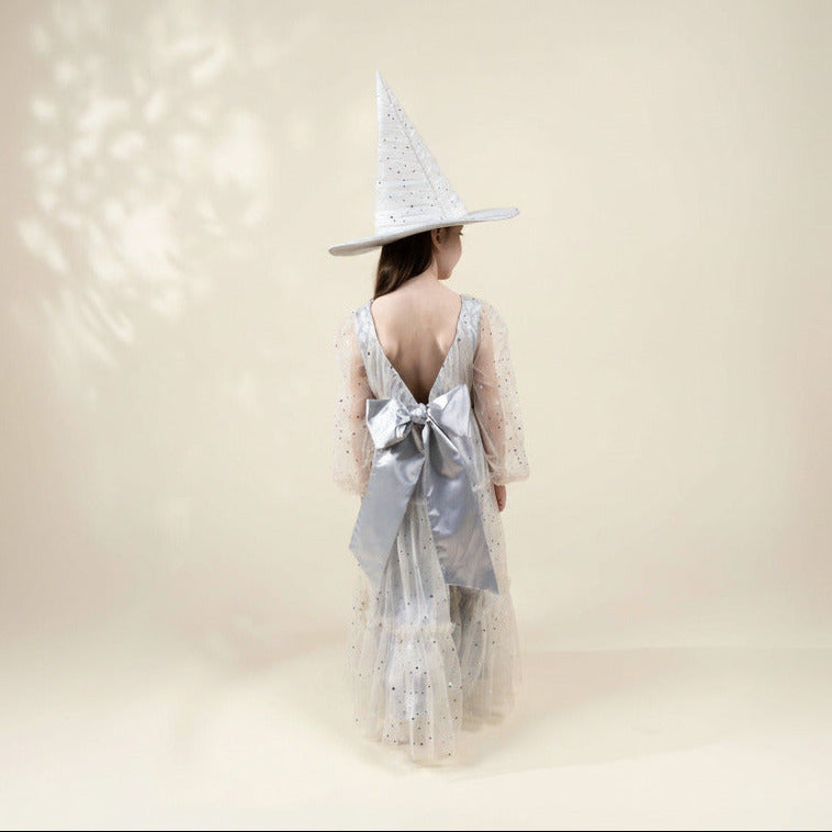 Person wearing a witch hat and dress with a large bow on a plain background