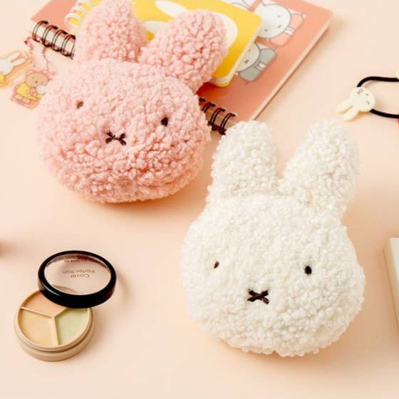 Two fluffy bunny-shaped pouches, one pink and one white, on a light pink background with stationery items.