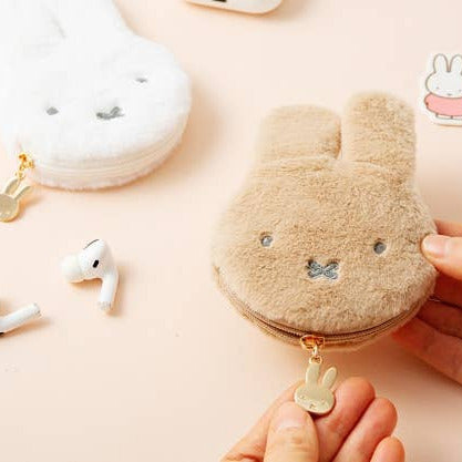 Fluffy beige pouch with bunny design held by a hand, with wireless earbuds and a white case in the background.