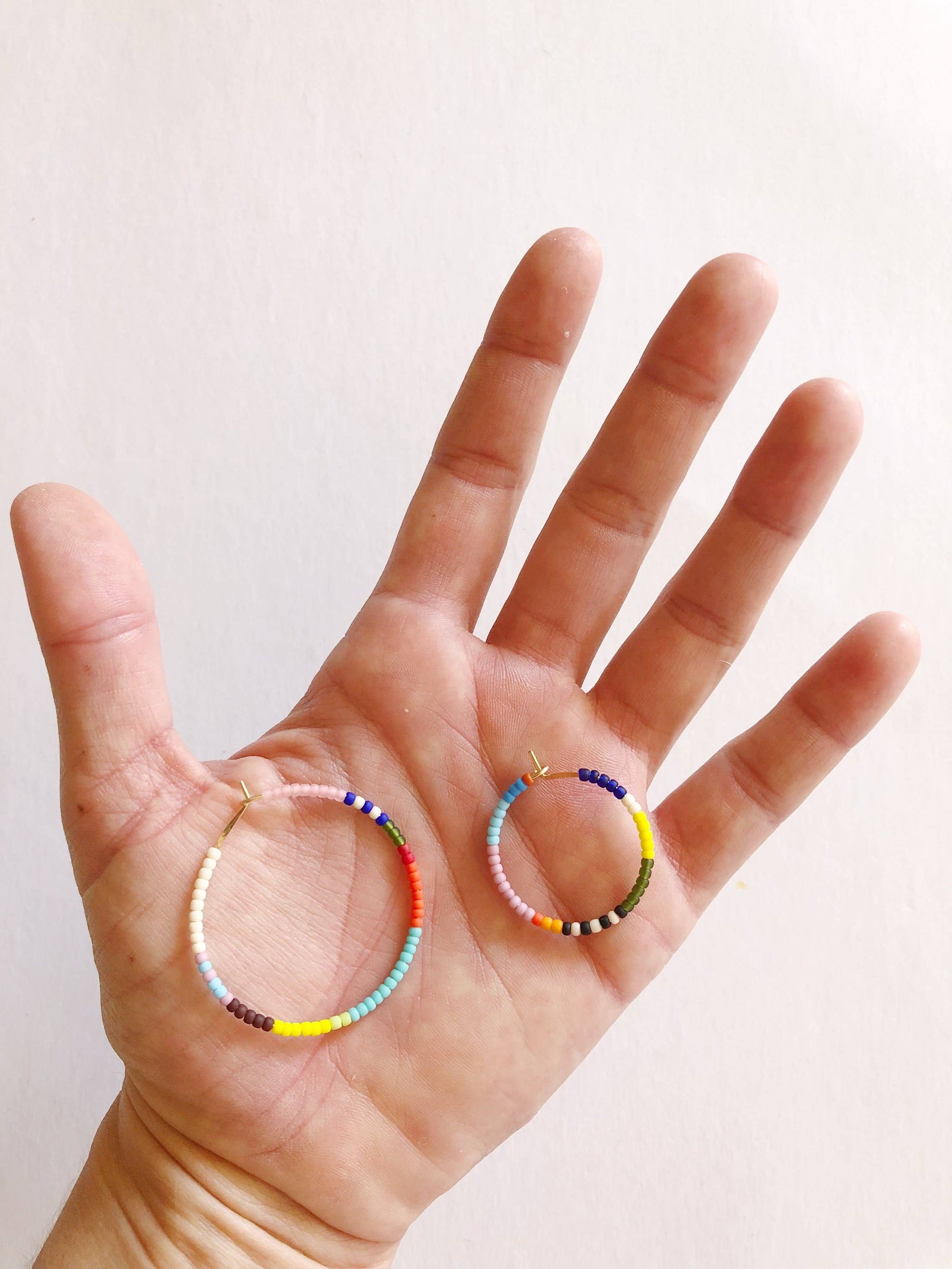 Hand wearing two colorful beaded rings on a plain background