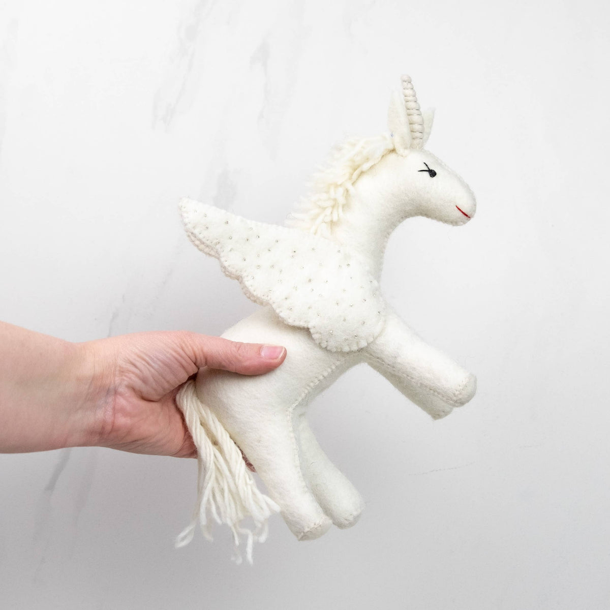 Hand holding a white unicorn toy against a plain background