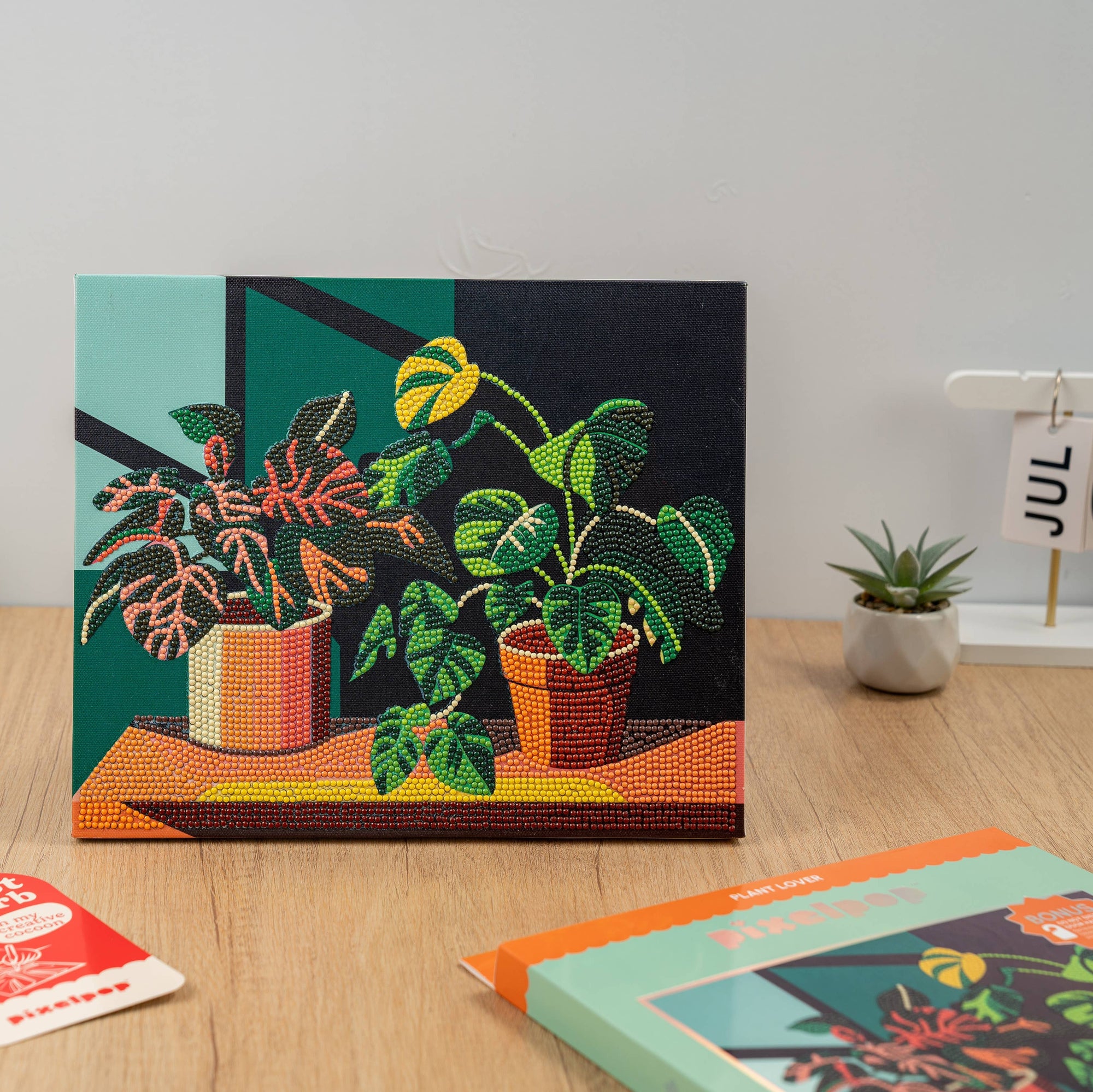 Decorative plant-themed wall art on a wooden surface with a calendar and small plants in the background.