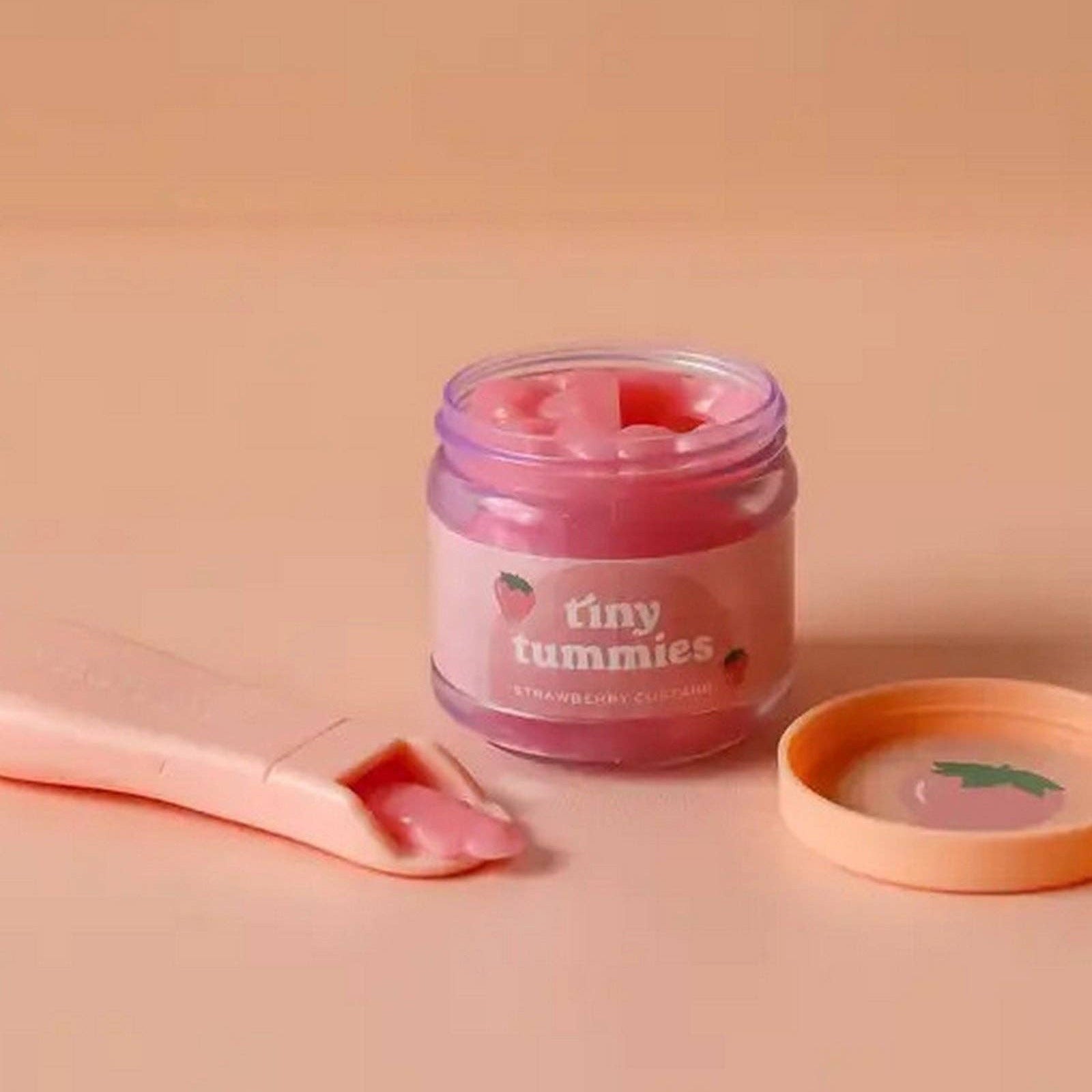 Jar of pink cream labeled 'tiny tummies' on a beige background