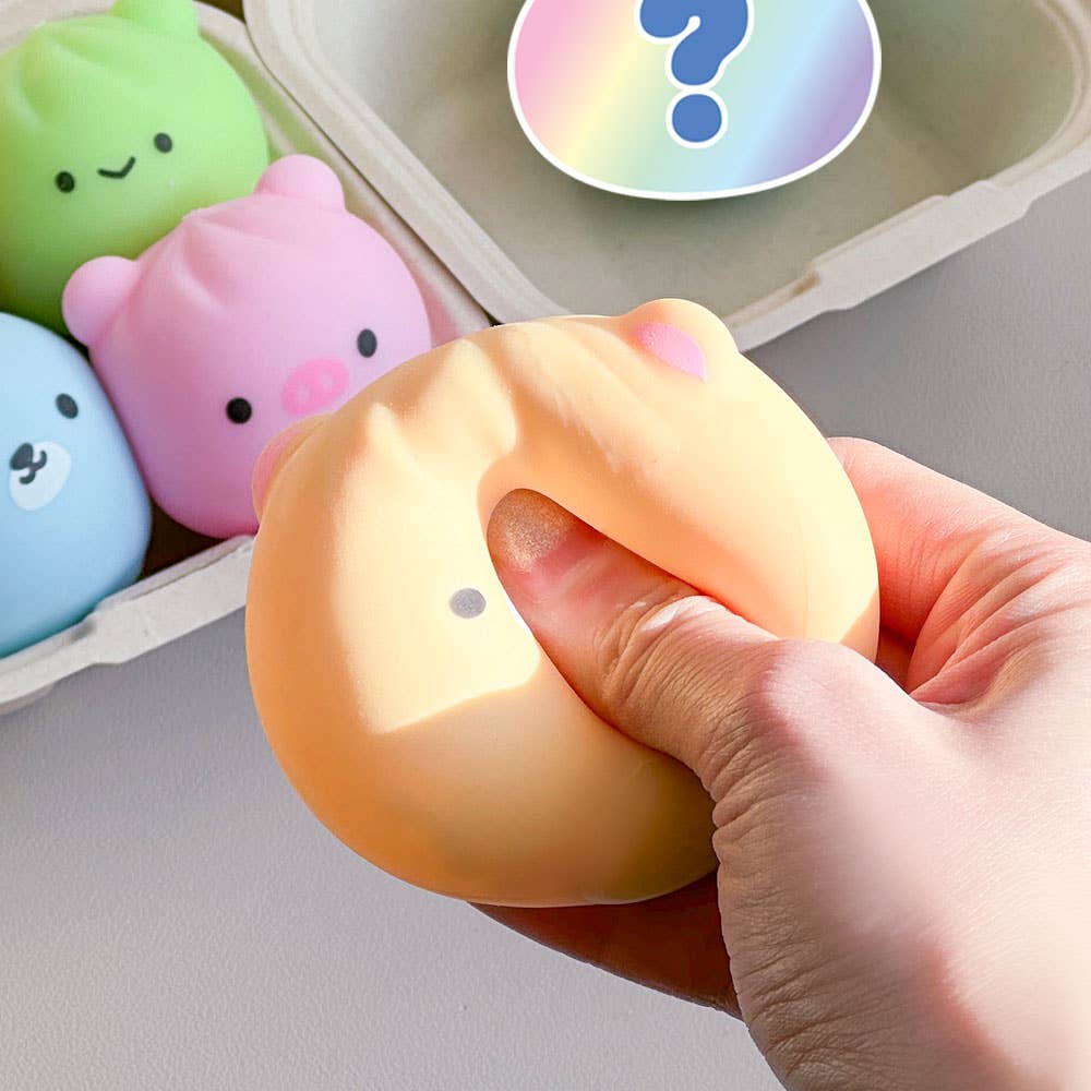 Hand holding a small yellow plush toy with a question mark above it, surrounded by other colorful plush toys in the background.