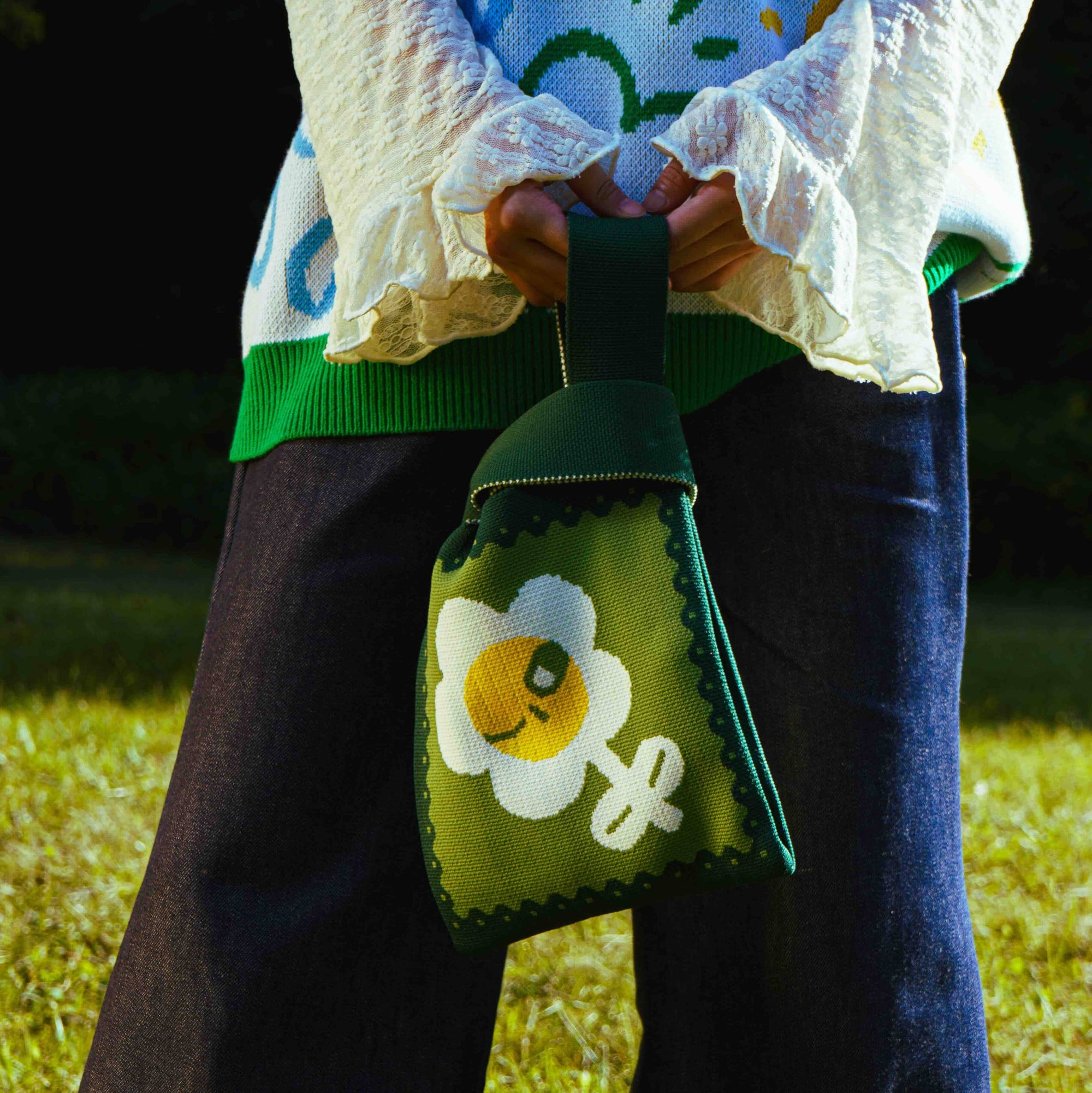 Person holding a green pouch with a floral design in a grassy outdoor setting