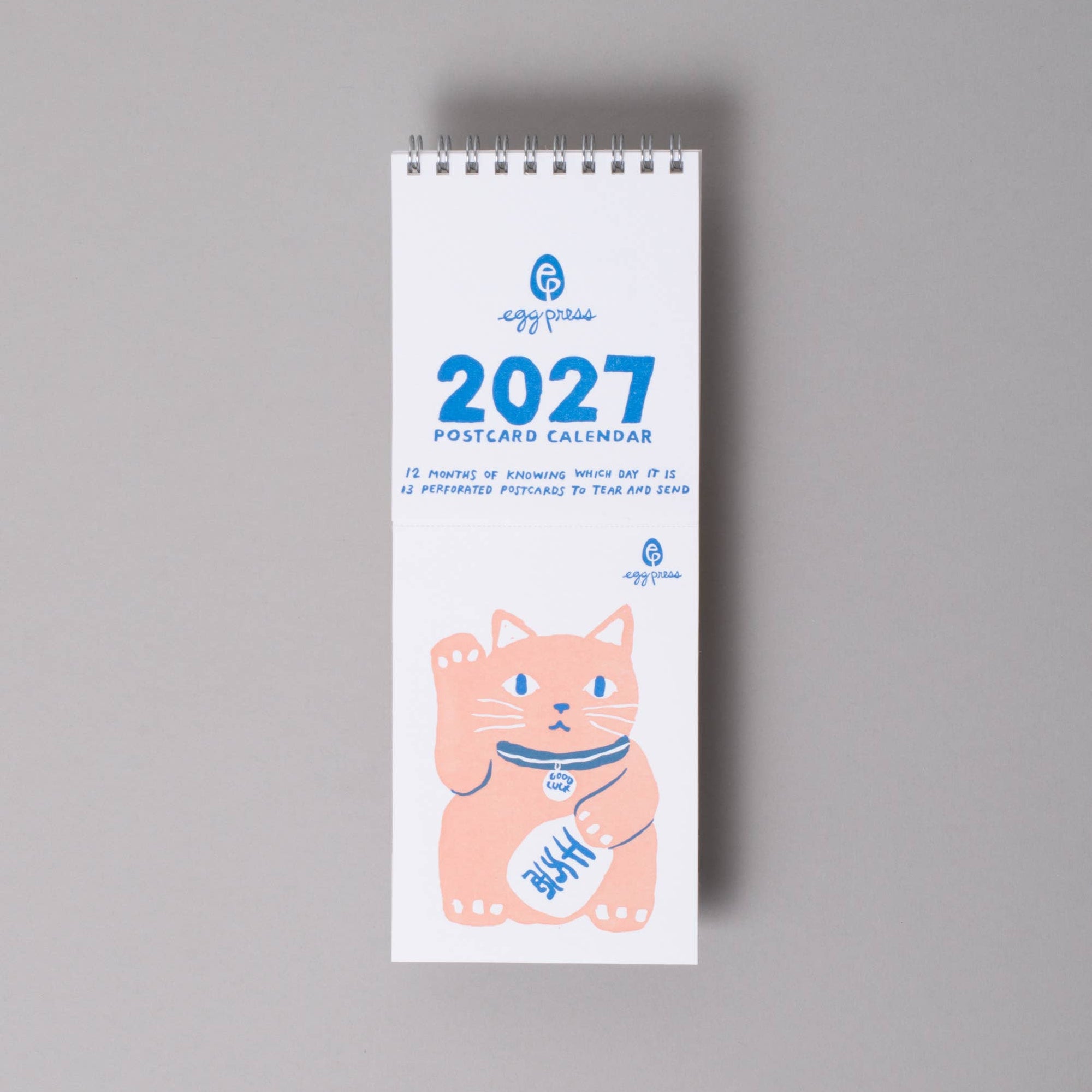 A vertical 2027 desk calendar from the brand 'appy times' featuring a cute pink cat illustration on a white background, photographed against a neutral gray wall.