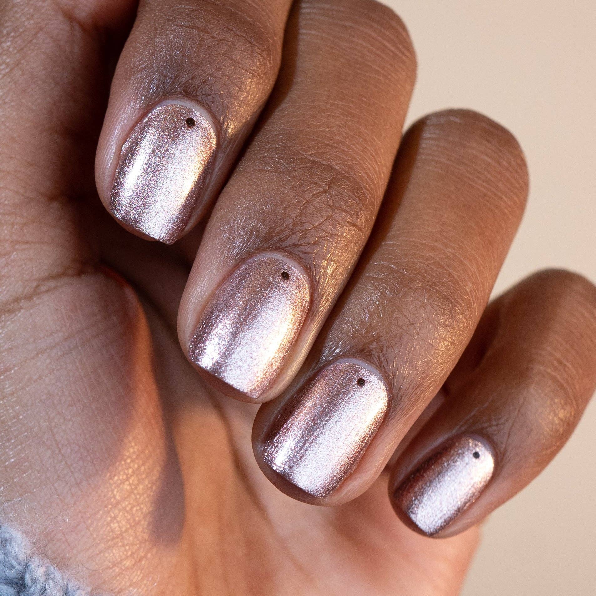 Hand with metallic nail polish on a neutral background