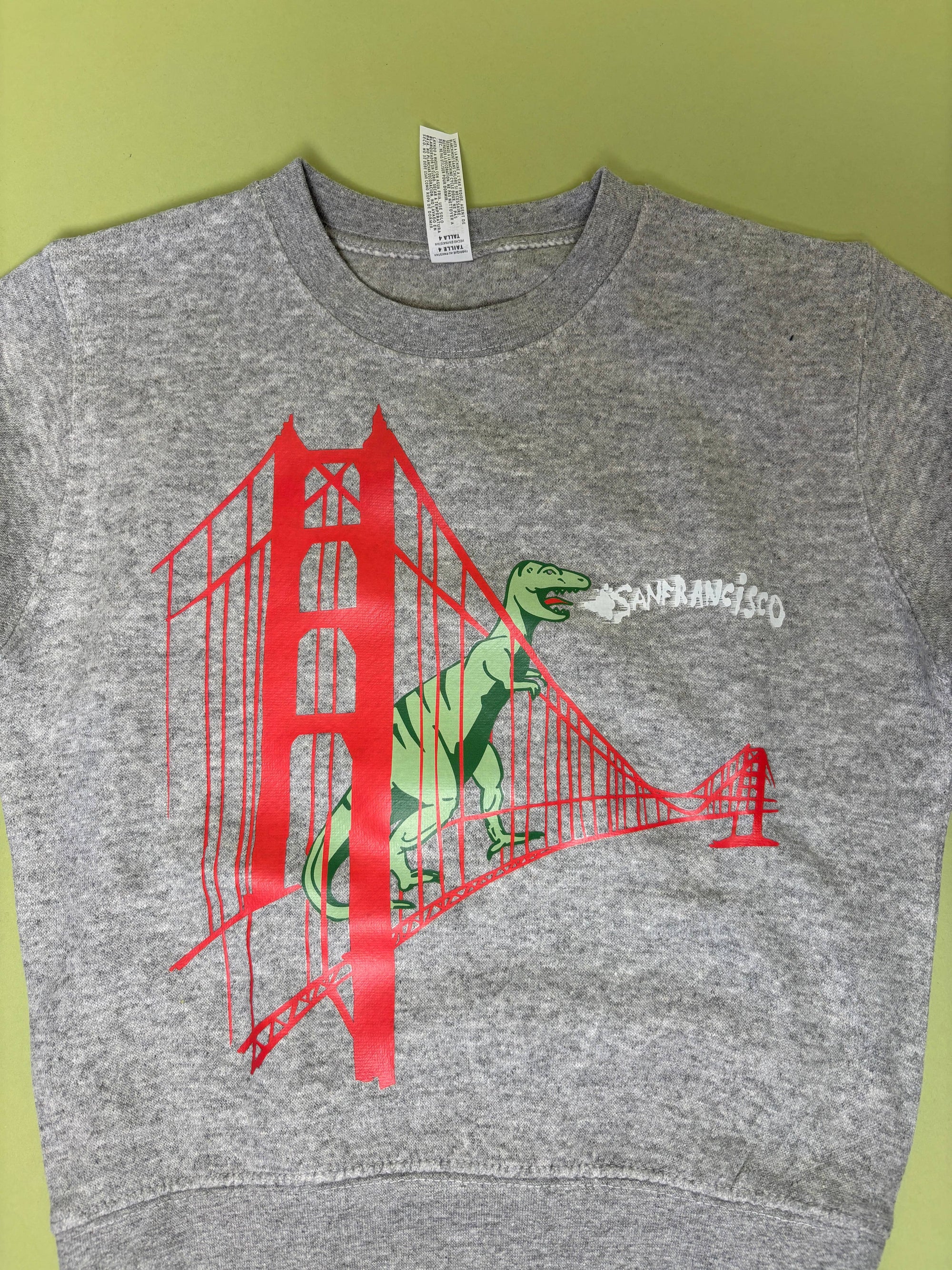 Gray sweatshirt with red Golden Gate Bridge and green dinosaur graphic on a green background