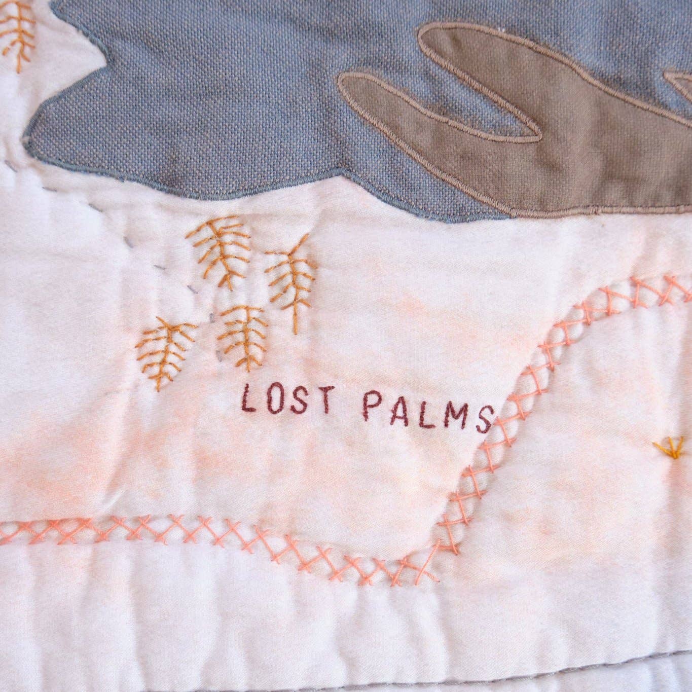 Textile art piece with embroidered text 'Lost Palms' on a fabric background.