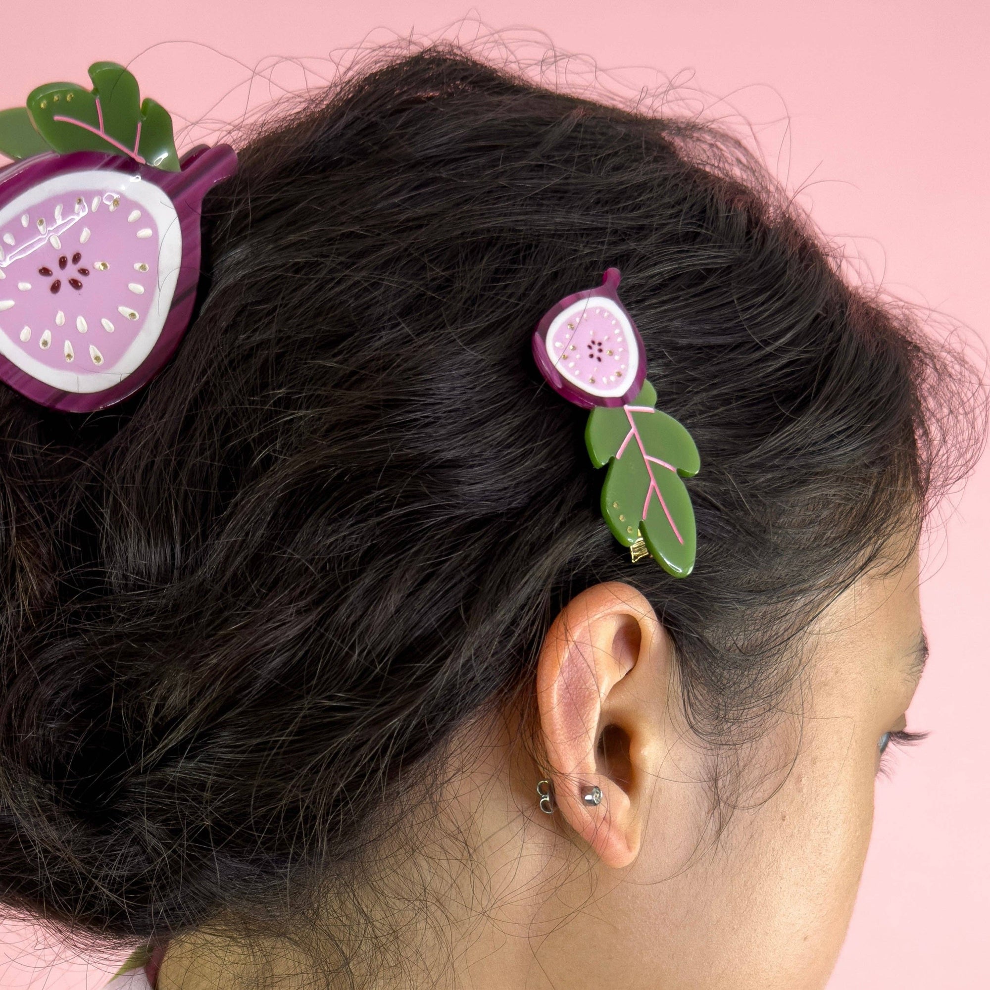 Hair accessories shaped like figs with leaves on a person's hair against a pink background