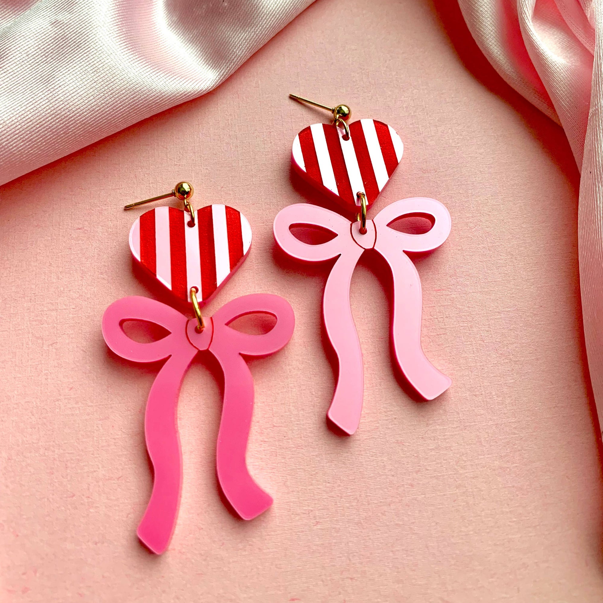 Pink bow and striped heart earrings on a pink satin background