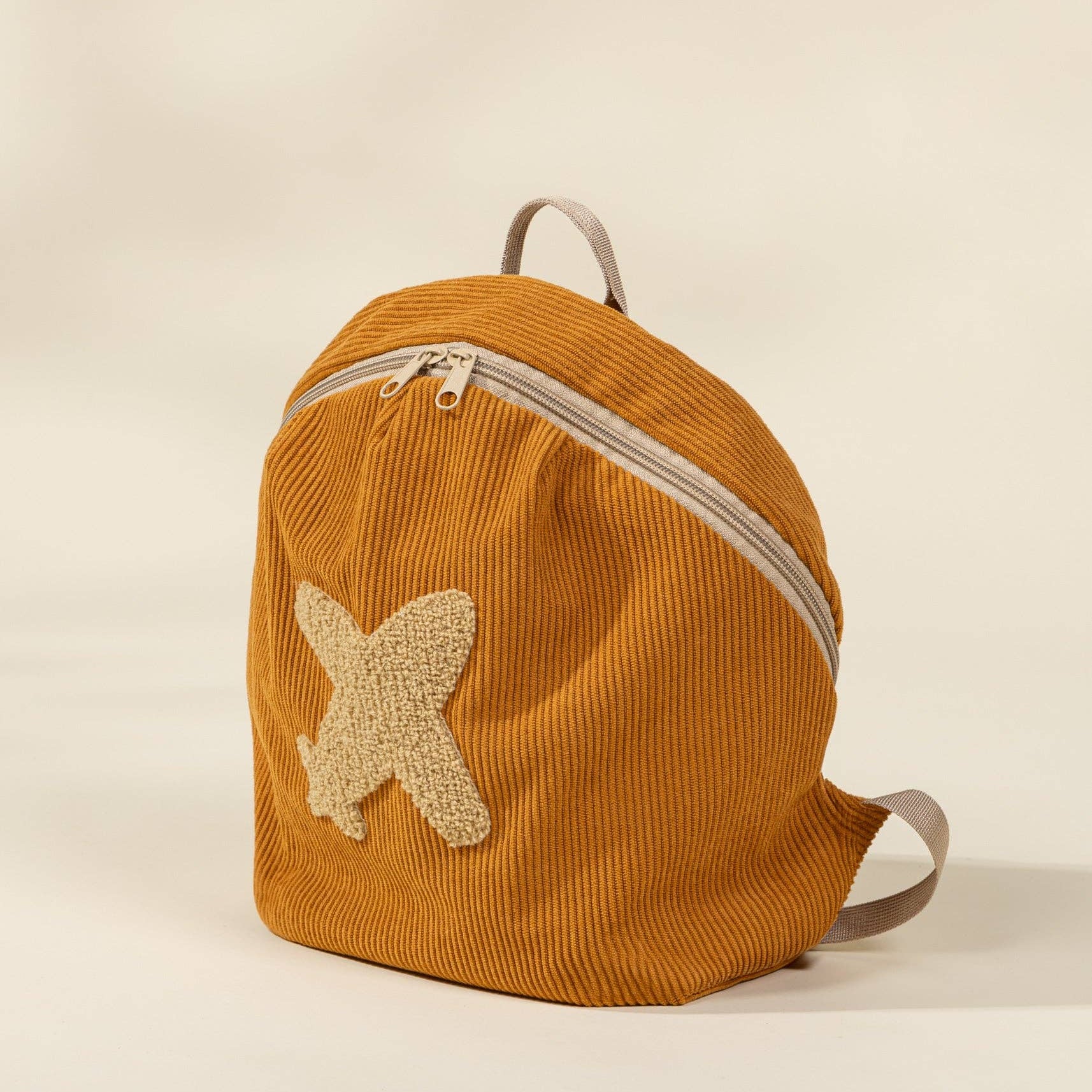 Yellow corduroy backpack with a butterfly patch on a beige background