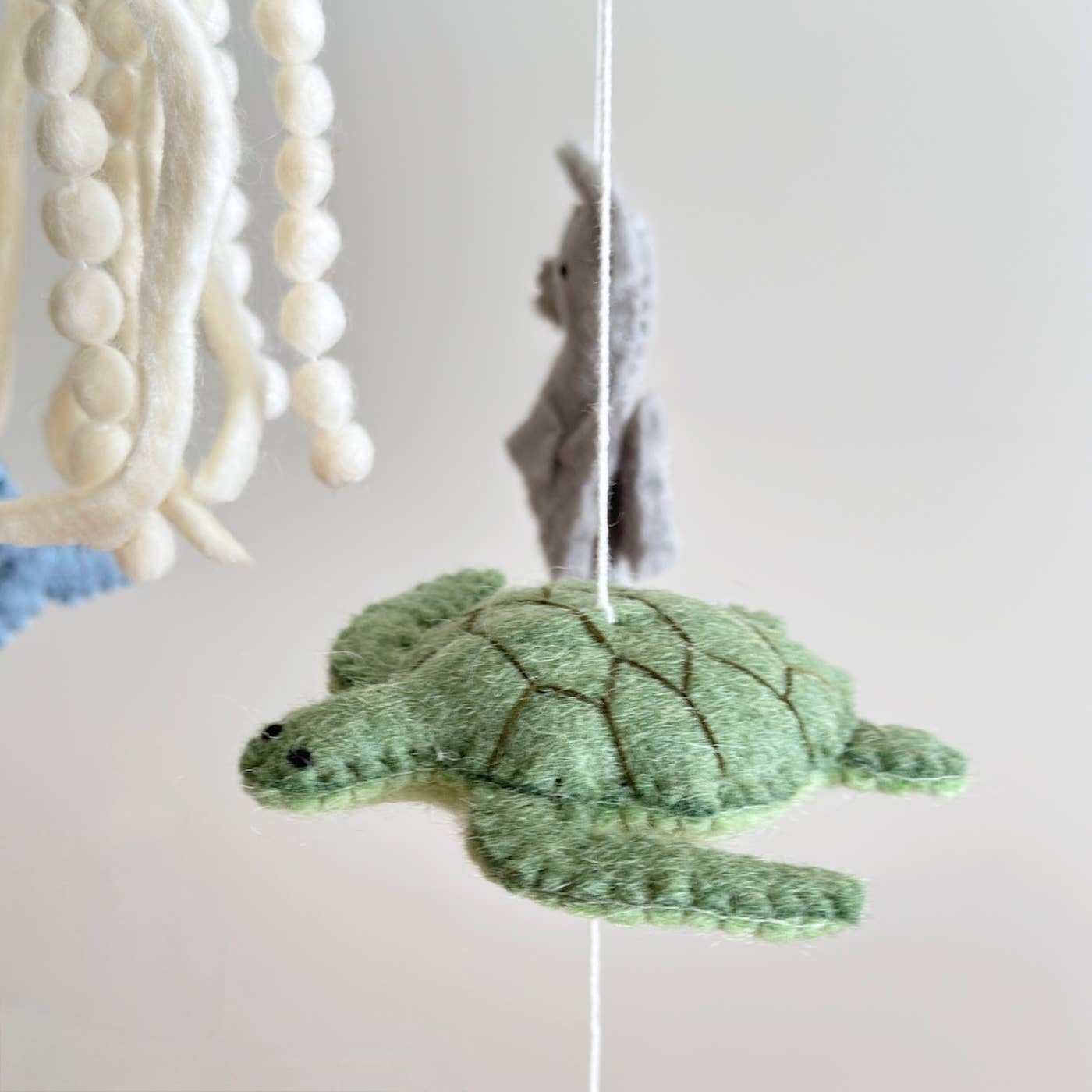 Green turtle toy hanging from a mobile with beads and yarn on a light background