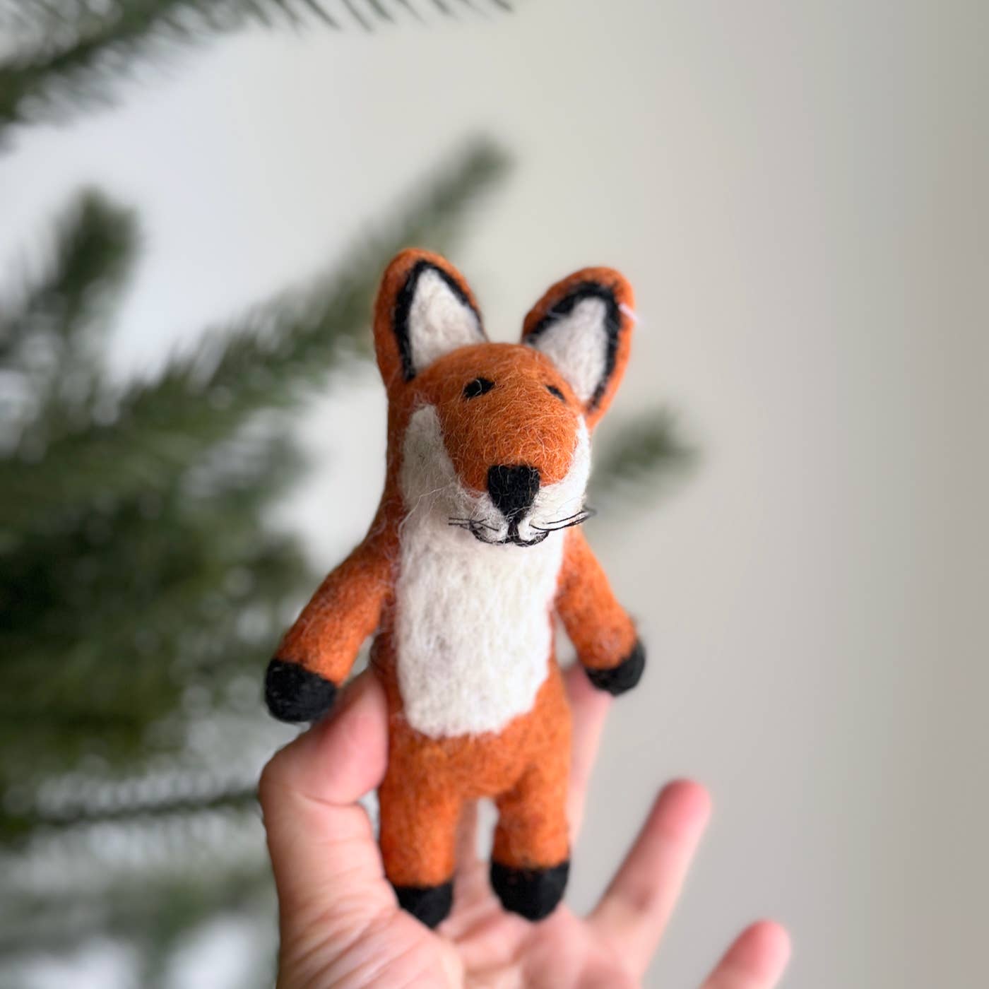 Hand holding a small fox plush toy with a blurred green background