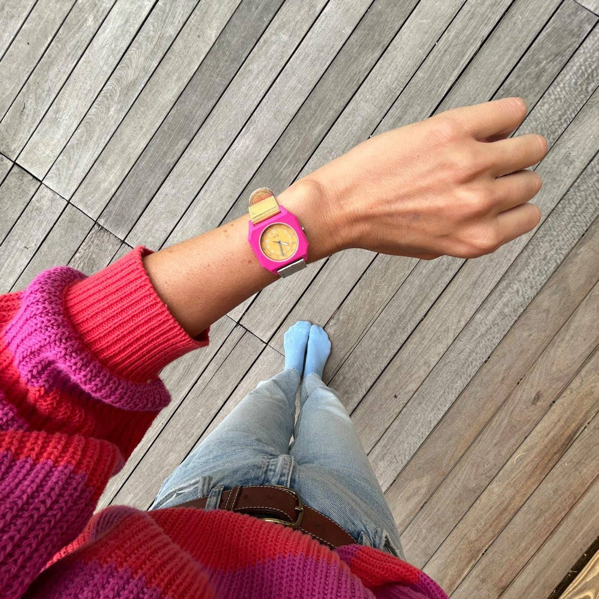 Person wearing a colorful sweater and pink watch on a wooden deck