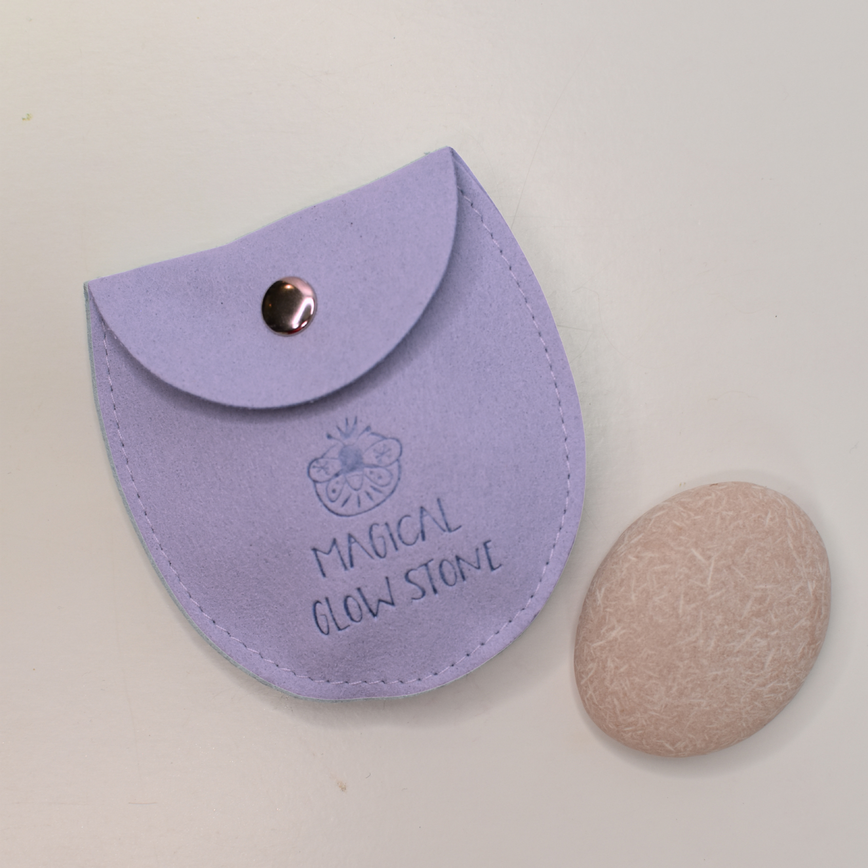 Purple pouch labeled 'Magical Glow Stone' with a beige stone on a light gray background