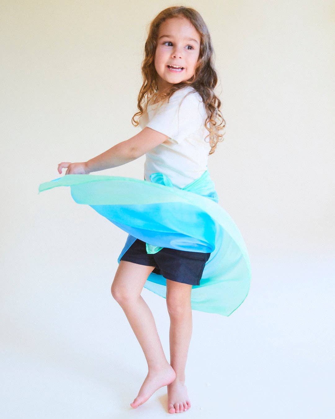 Young girl dancing with a blue and green skirt against a plain background