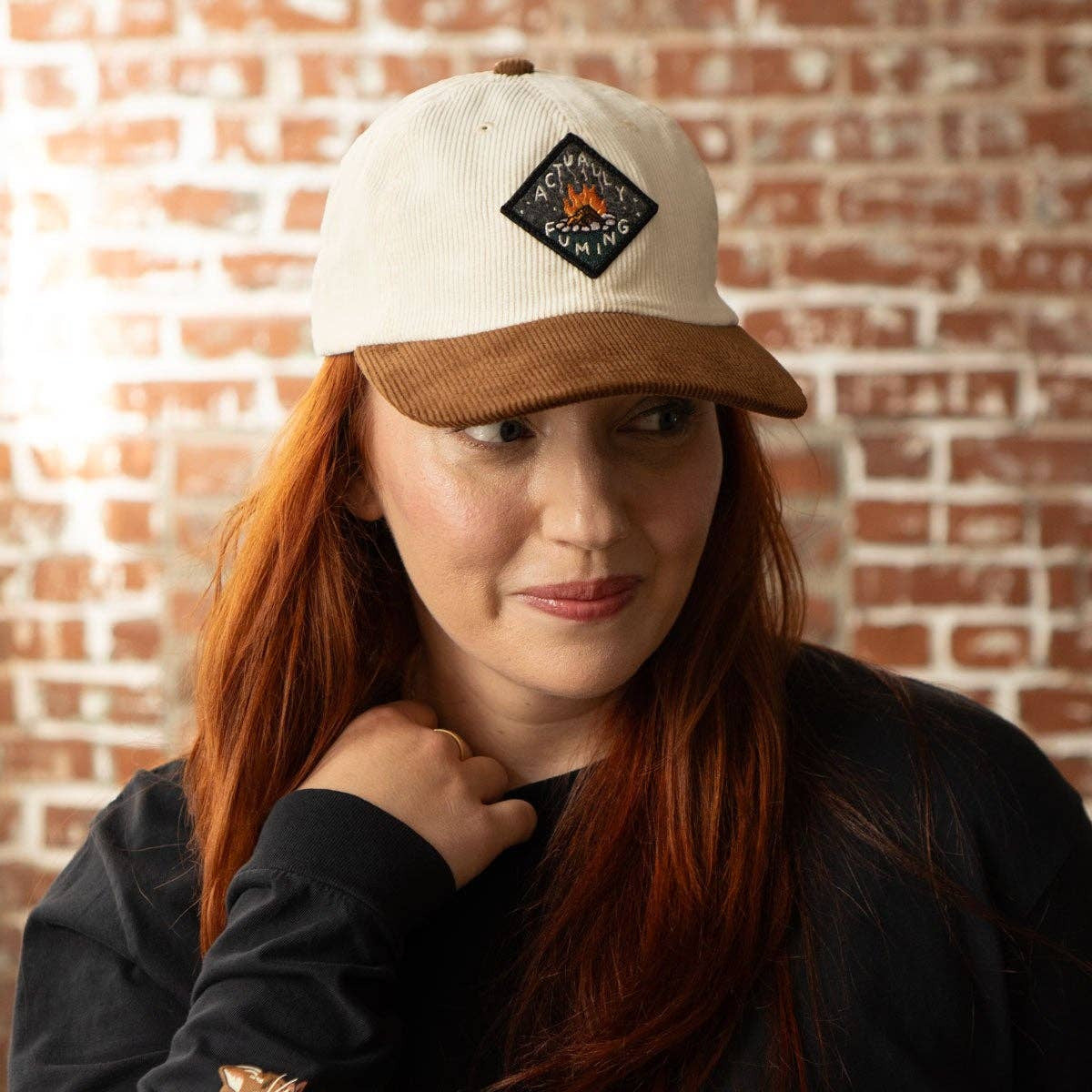 Woman wearing a white cap with a logo against a brick wall